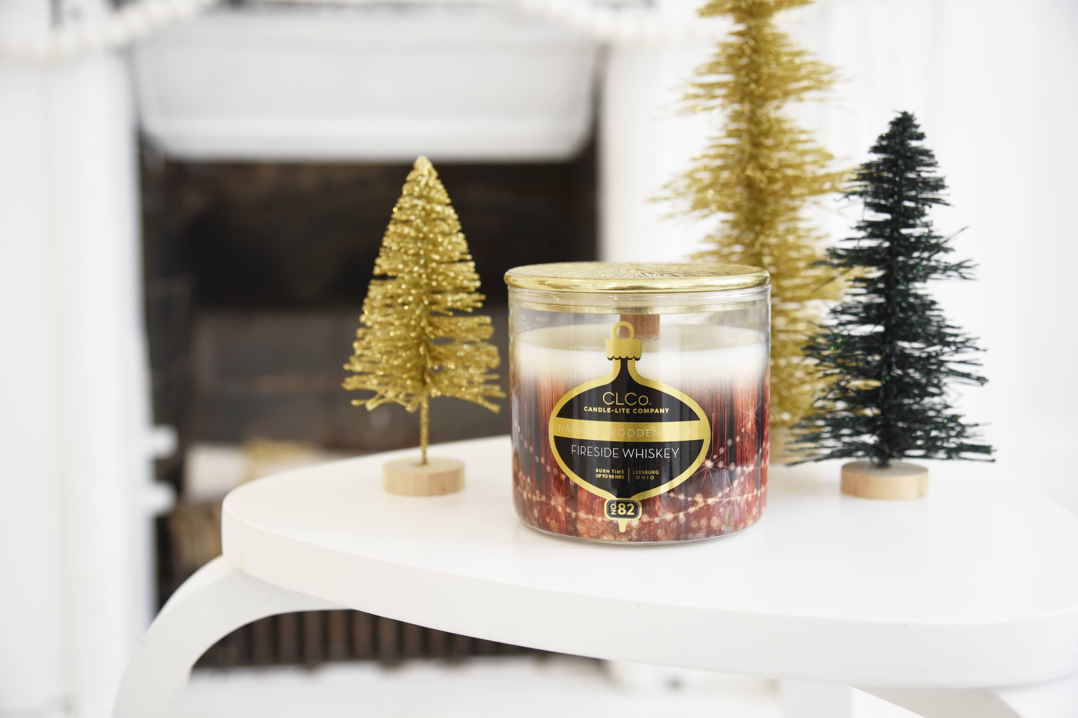 Candle with a bottle label design surrounded by small decorative trees on a white surface.